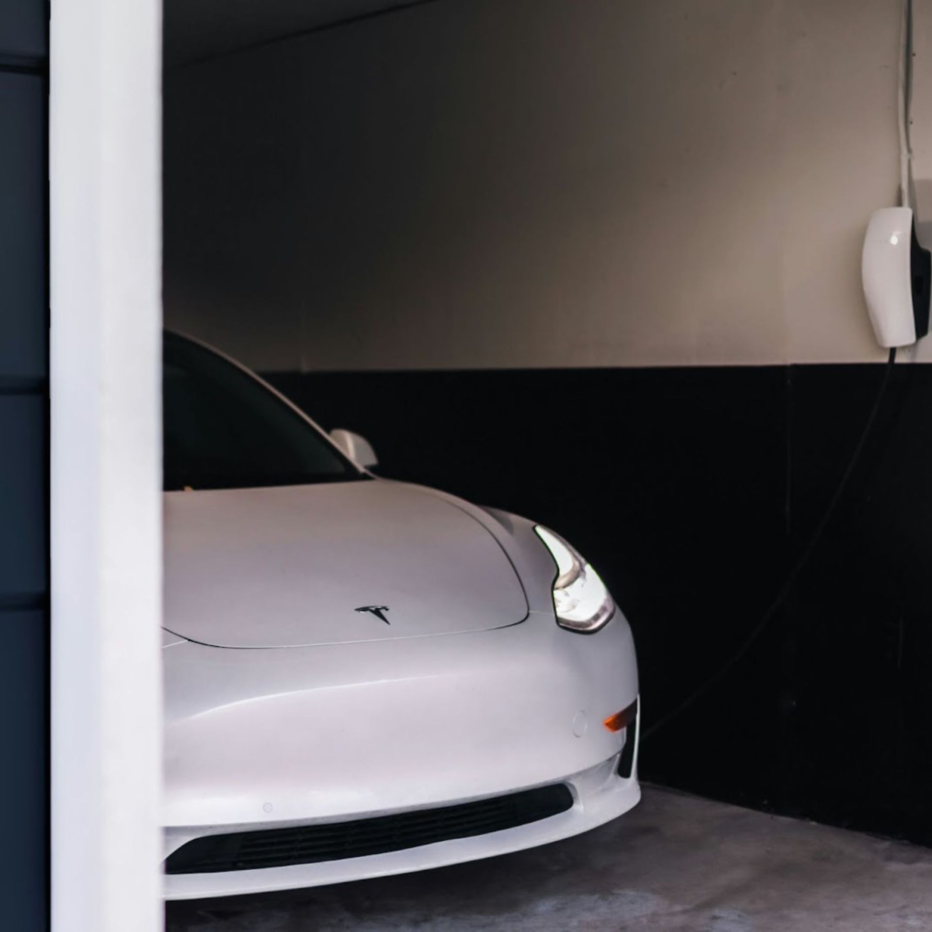White Tesla charger mounted on a beige wall with a black cable and plug visible.