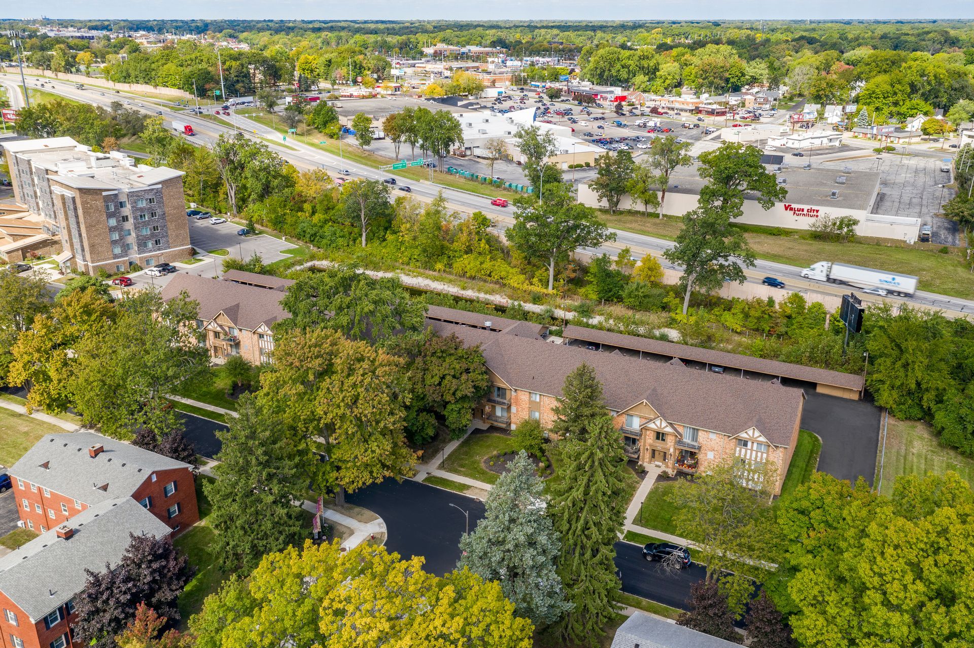 Aerial view of apartment buildings with surrounding trees and a highway, sunny day.