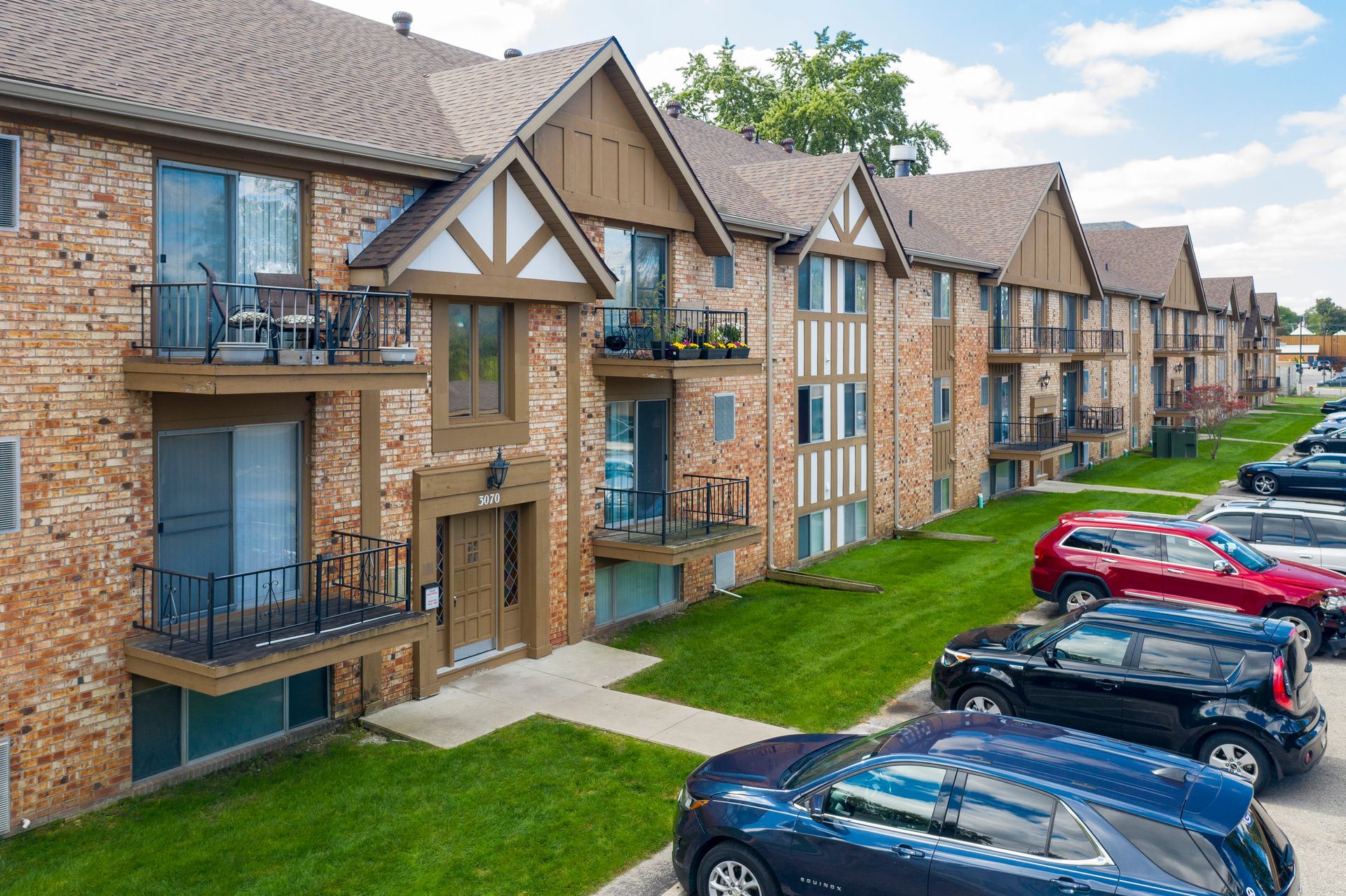 Apartment building with brick exterior, Tudor-style accents, balconies, and parked cars.