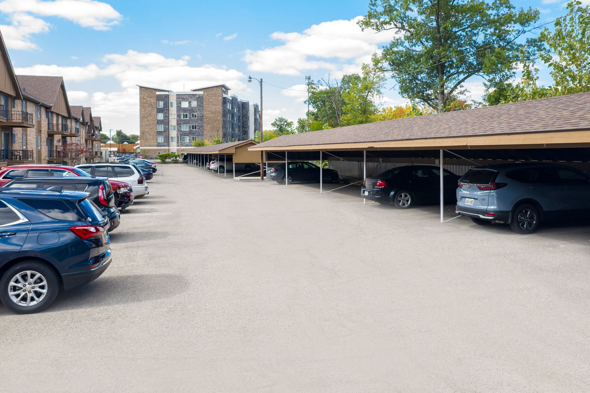 Parking lot with covered spaces; cars parked under brown awnings, buildings in the background.