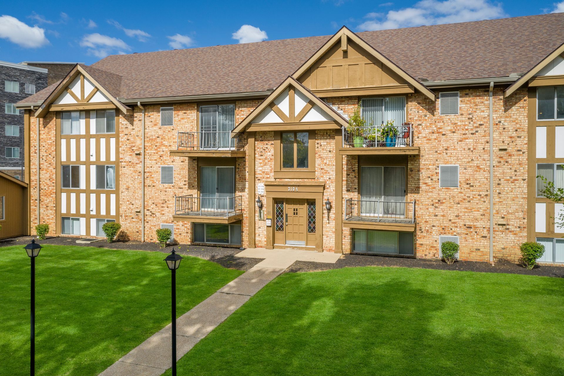 Apartment building with brown roof and brick exterior, set in green lawn with walkway.
