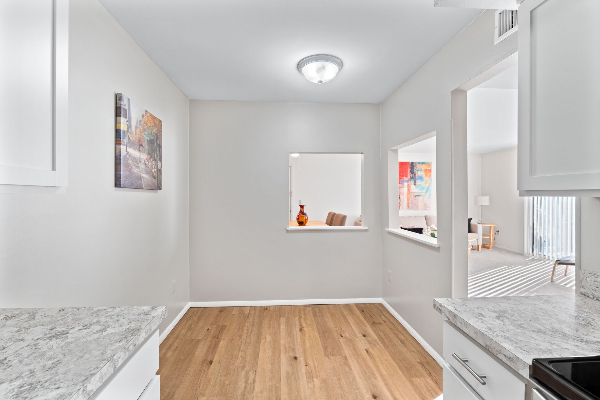 Dining room with wooden floor, light grey walls, and a small decorative painting.