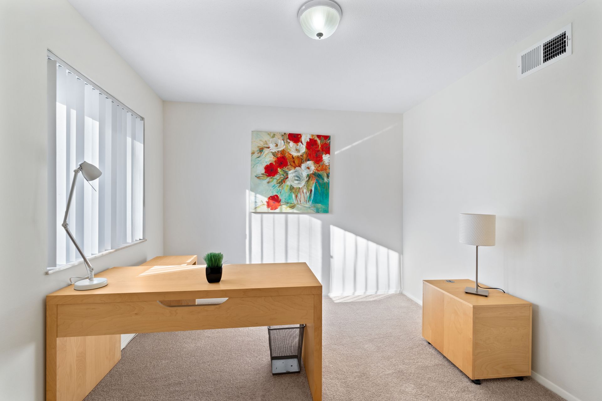 Bright office space with a desk, cabinet, artwork, and window with blinds.