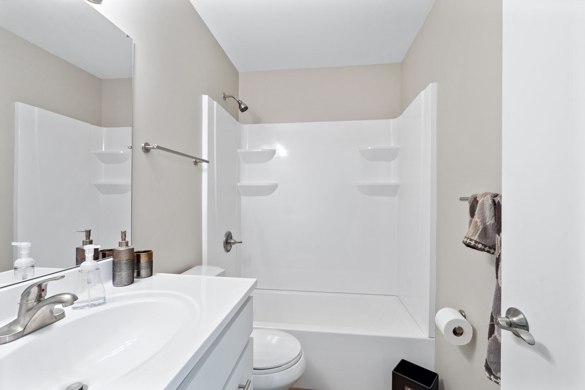 Bathroom with a white bathtub, toilet, and sink. Beige walls, silver fixtures, and decorative bottles.
