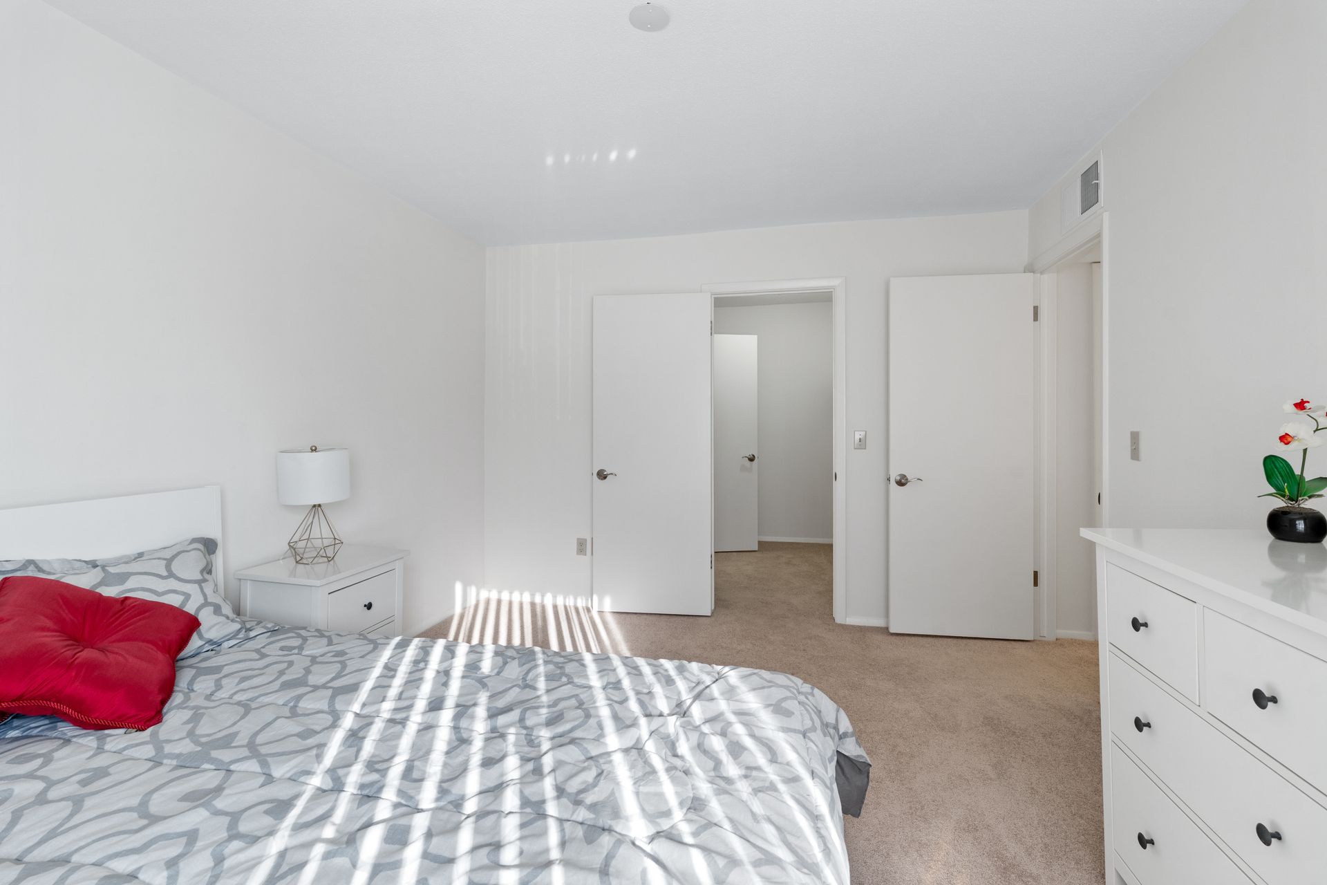 Bedroom with white walls, carpet, bed, dresser, and two closed doors.