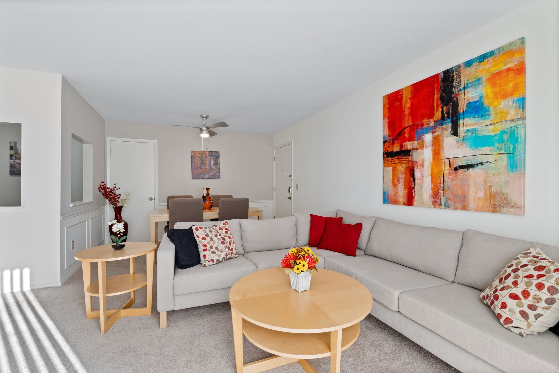 Living room with a sectional sofa, coffee table, and colorful abstract art on the wall.
