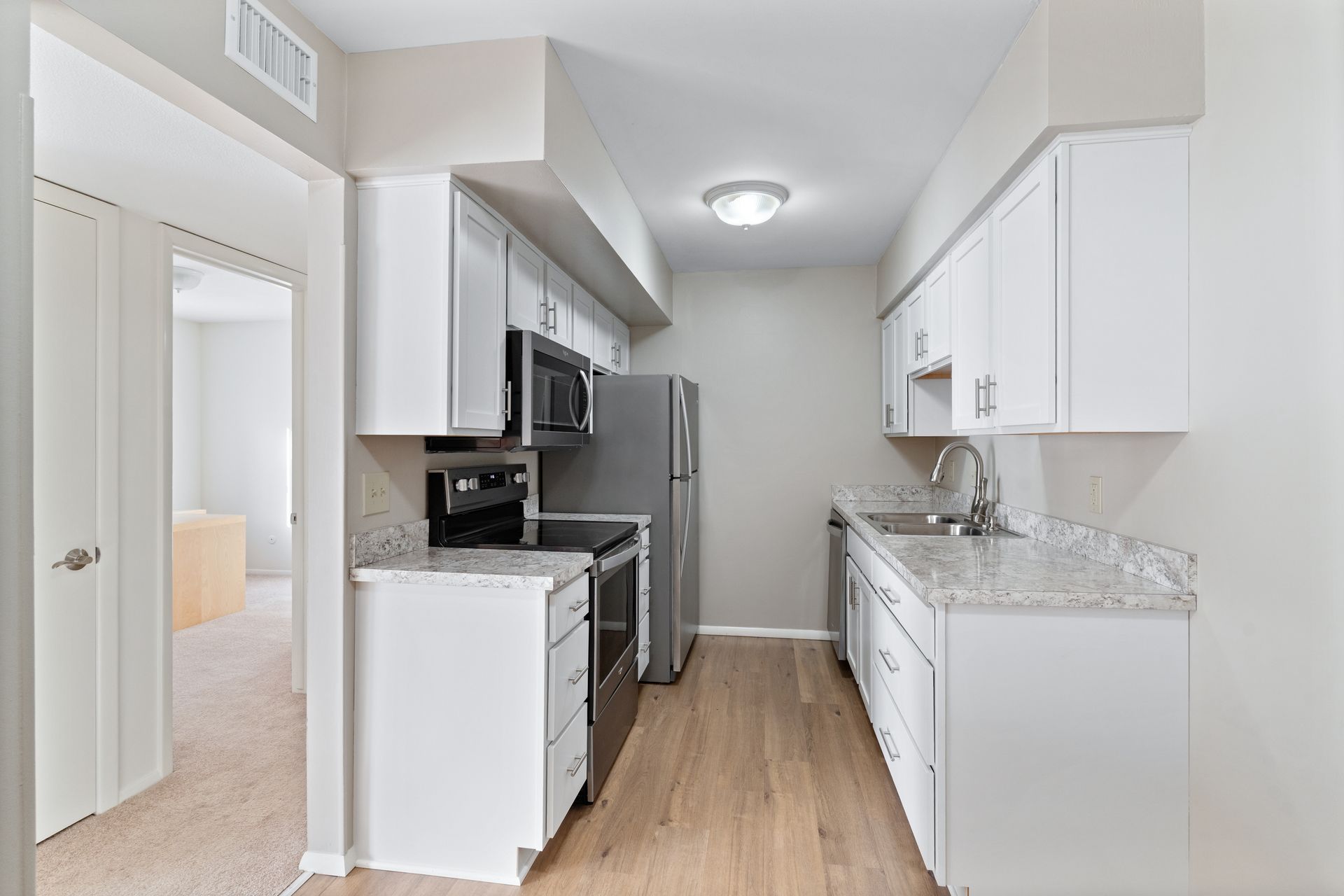 Small, renovated kitchen with white cabinets, stainless steel appliances, and light wood flooring.