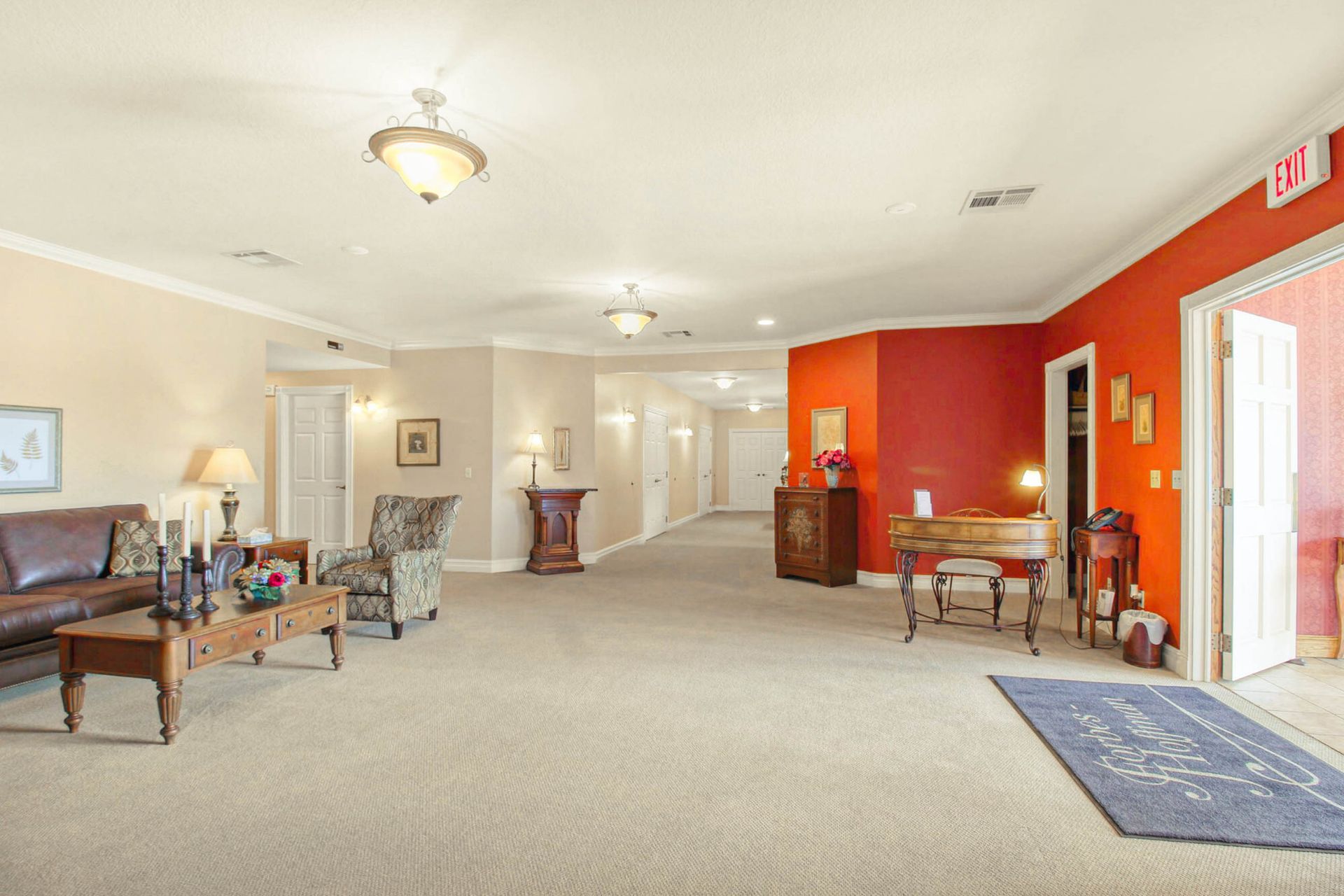 Spacious waiting room with seating, hallway, desk, and red accent wall. Beige walls and carpet.