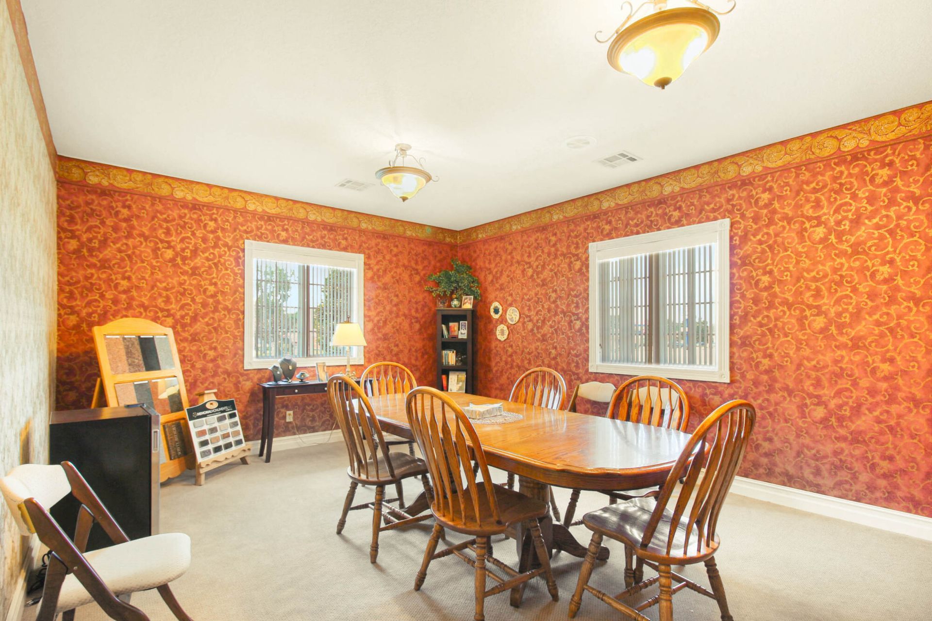 Dining room with oval table, wooden chairs, red patterned walls, and two windows.
