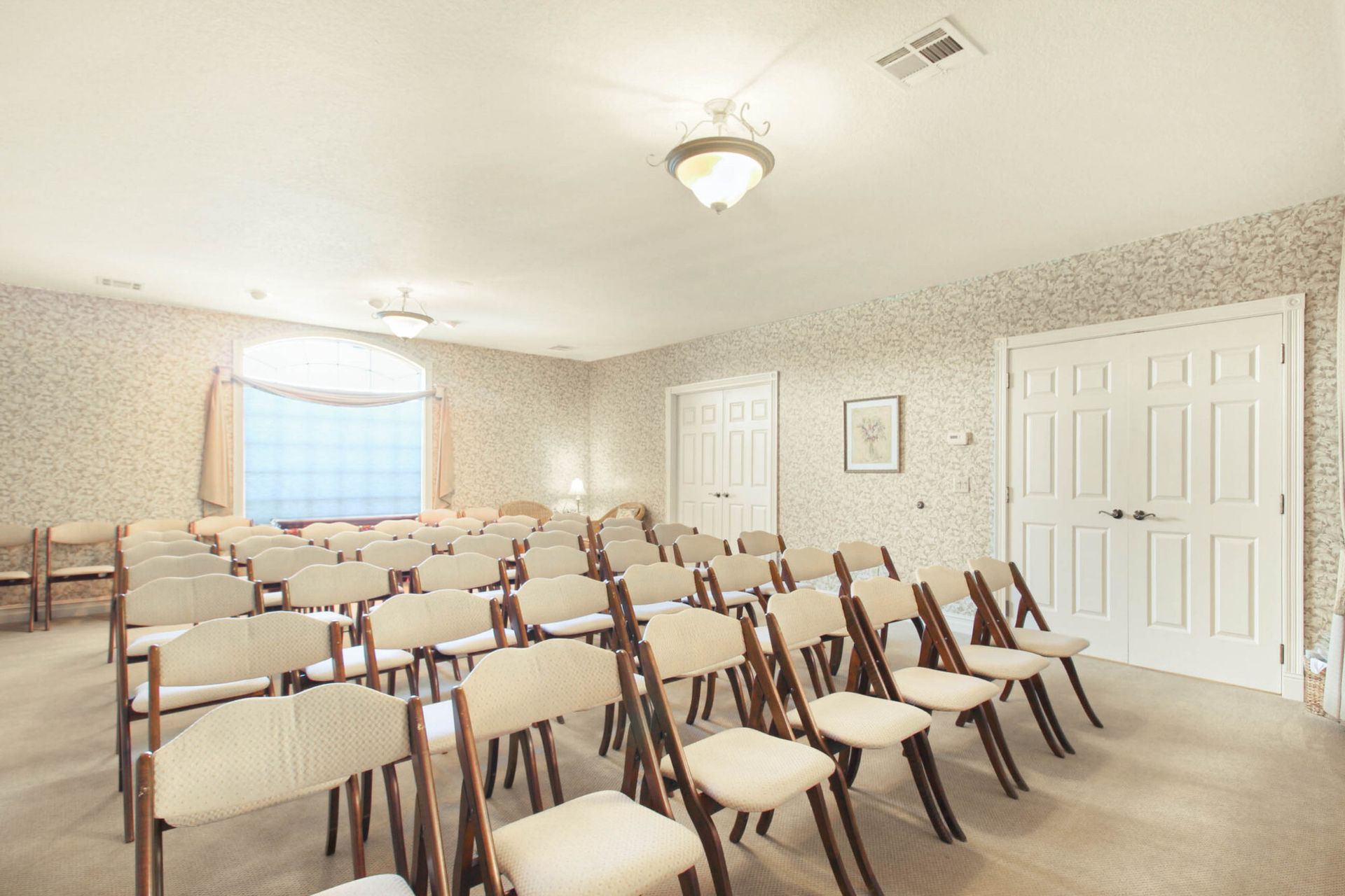 Empty room with rows of beige chairs, two doors, and patterned wallpaper.