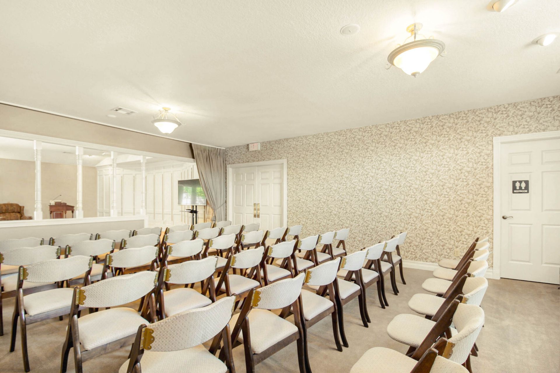 Rows of white chairs face a stage in a room with patterned walls and doors.