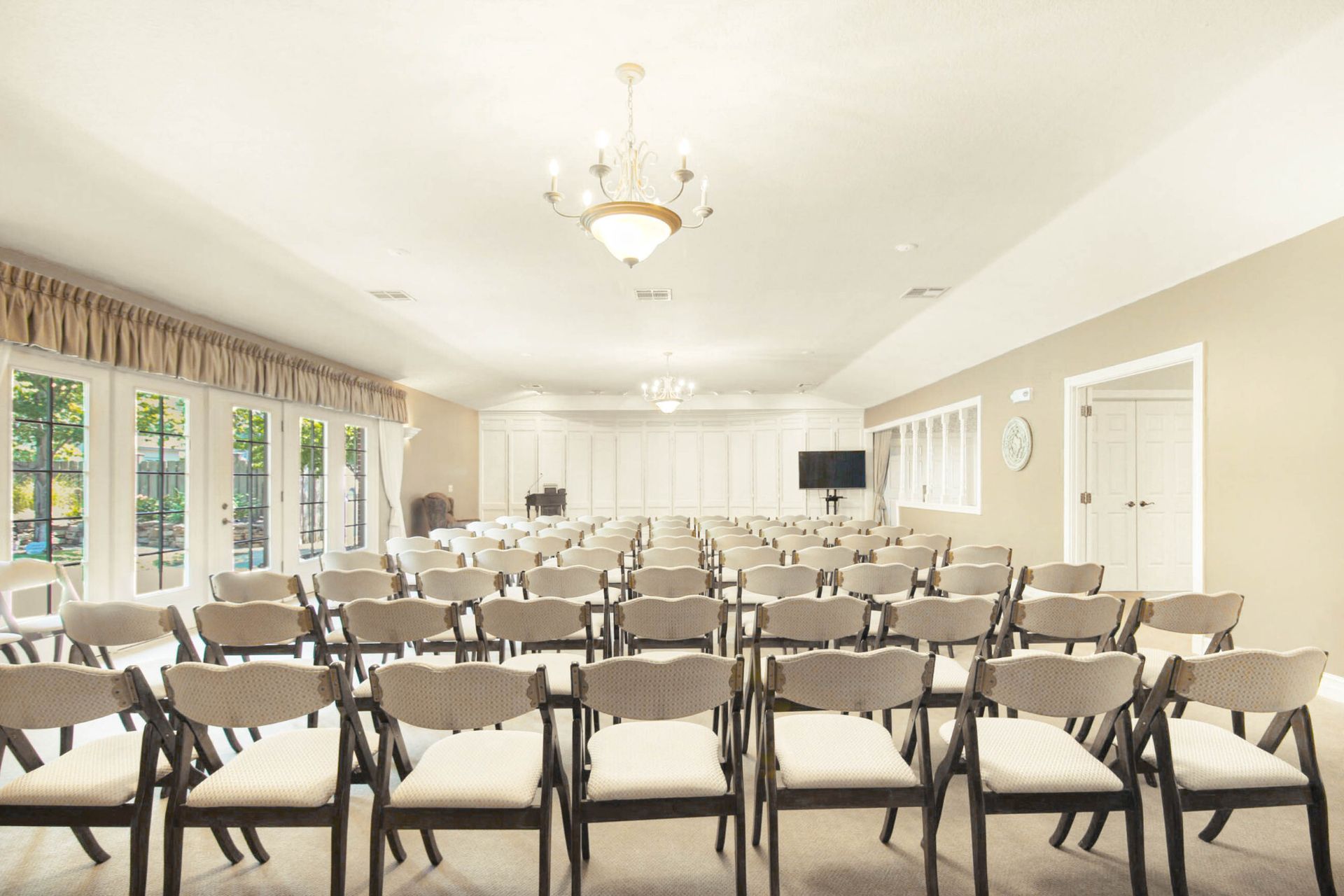 Empty event space with rows of chairs, large windows, chandelier, and a TV.