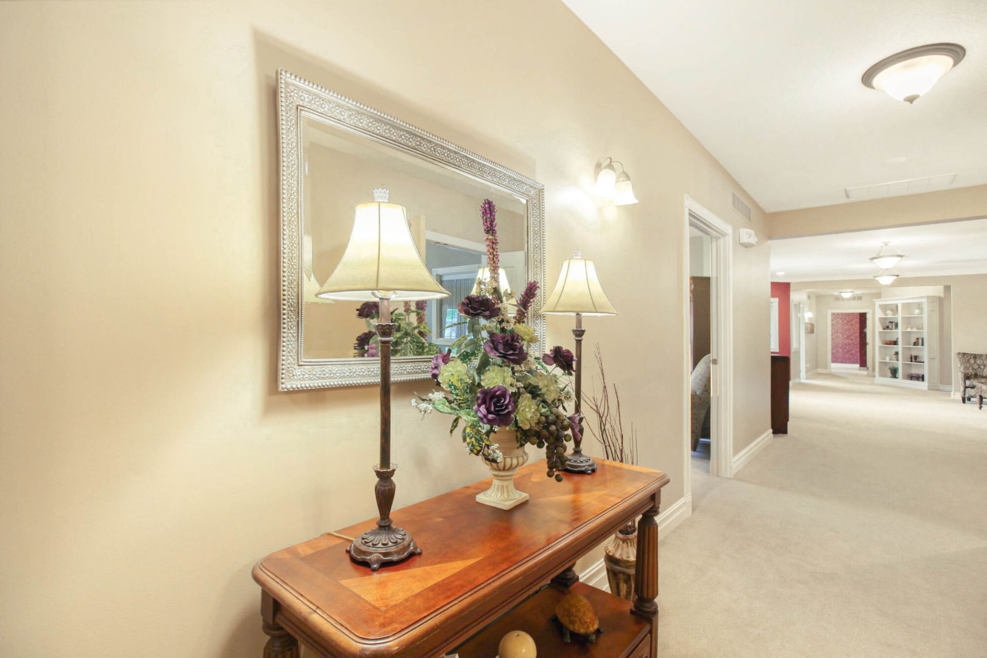 Hallway with console table holding lamps and floral arrangement, a large mirror, and neutral walls.