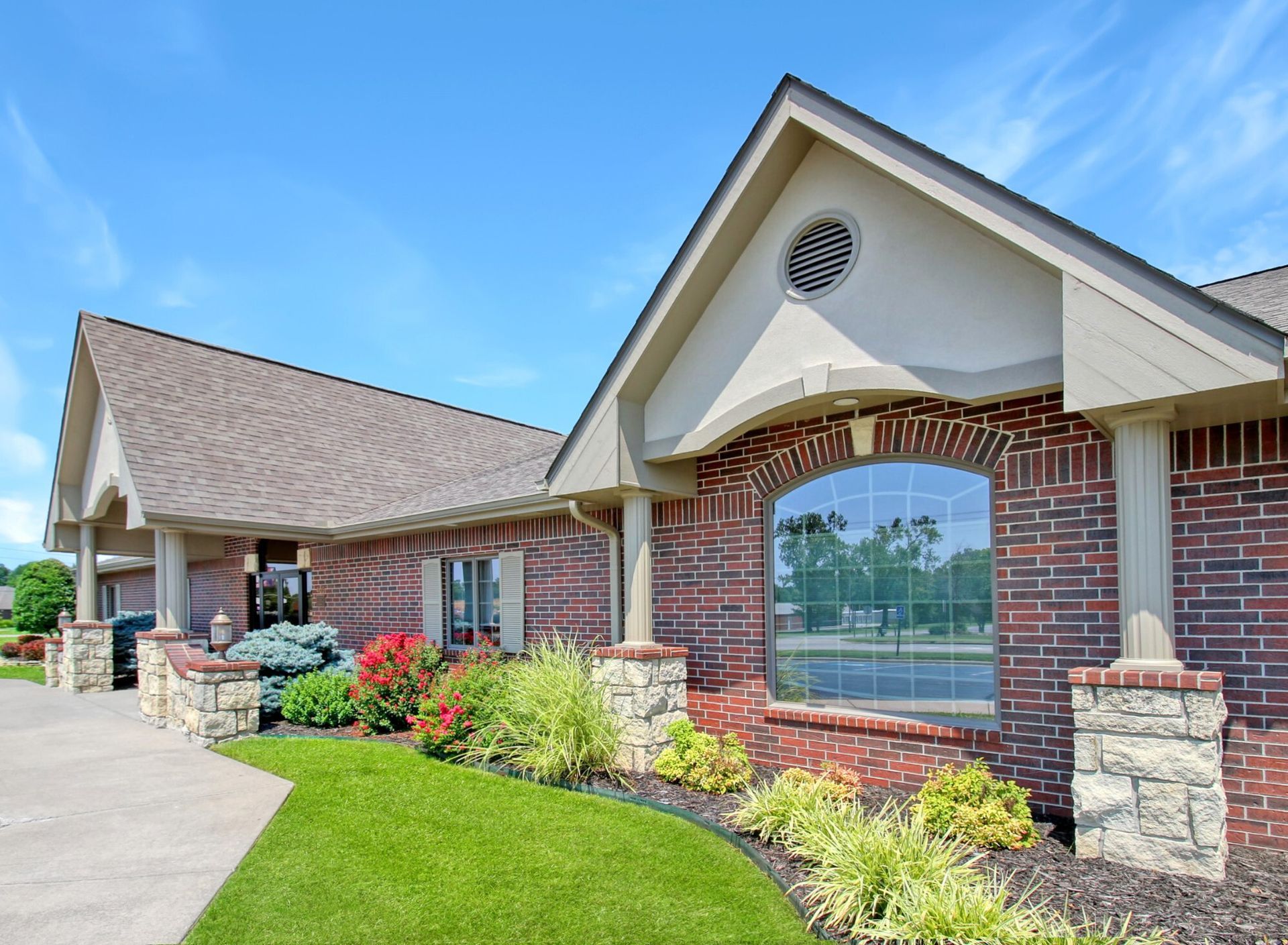 Brick building with a green lawn and colorful landscaping under a blue sky.