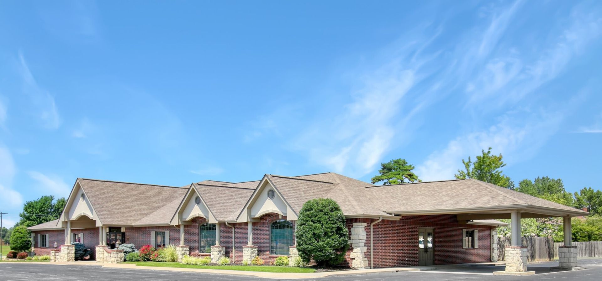 A single-story brick building with a brown roof under a blue sky with a few clouds.