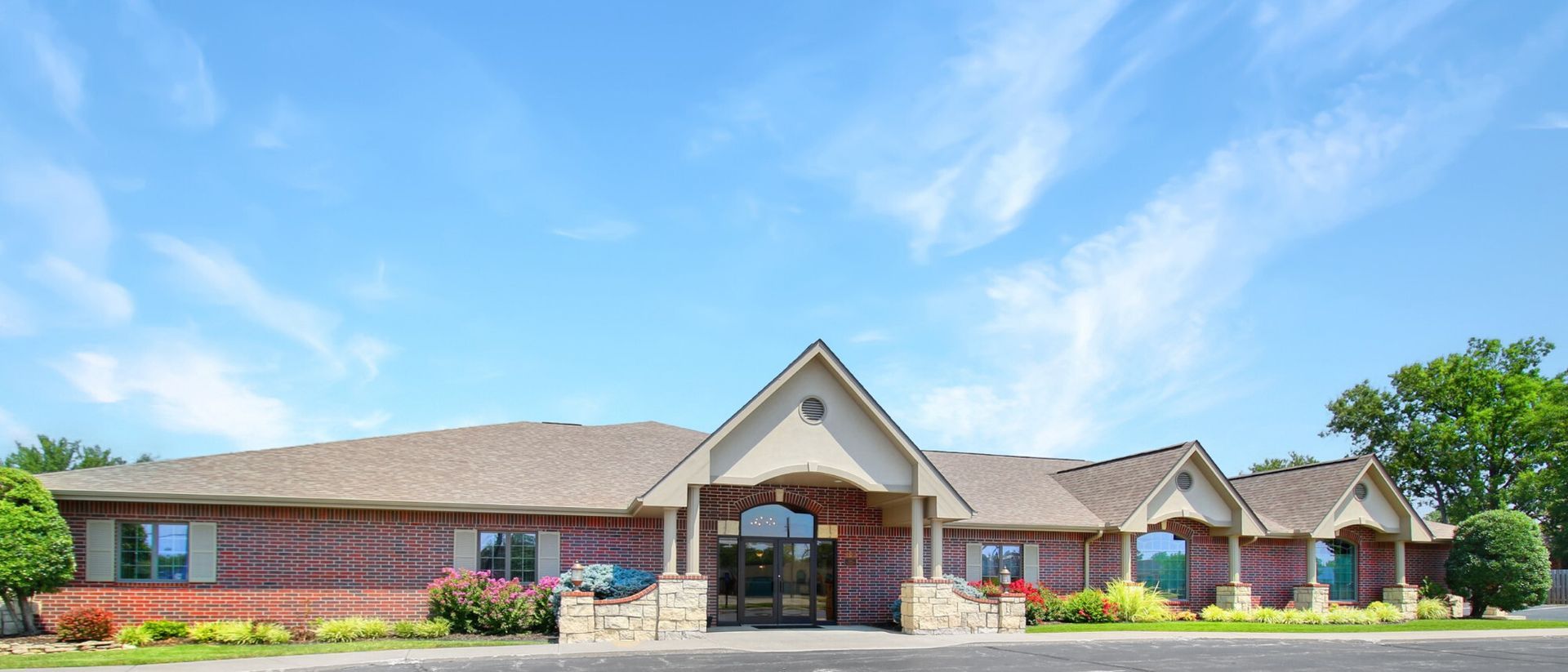 Brick building with a gabled entrance, windows, and a blue sky with clouds.