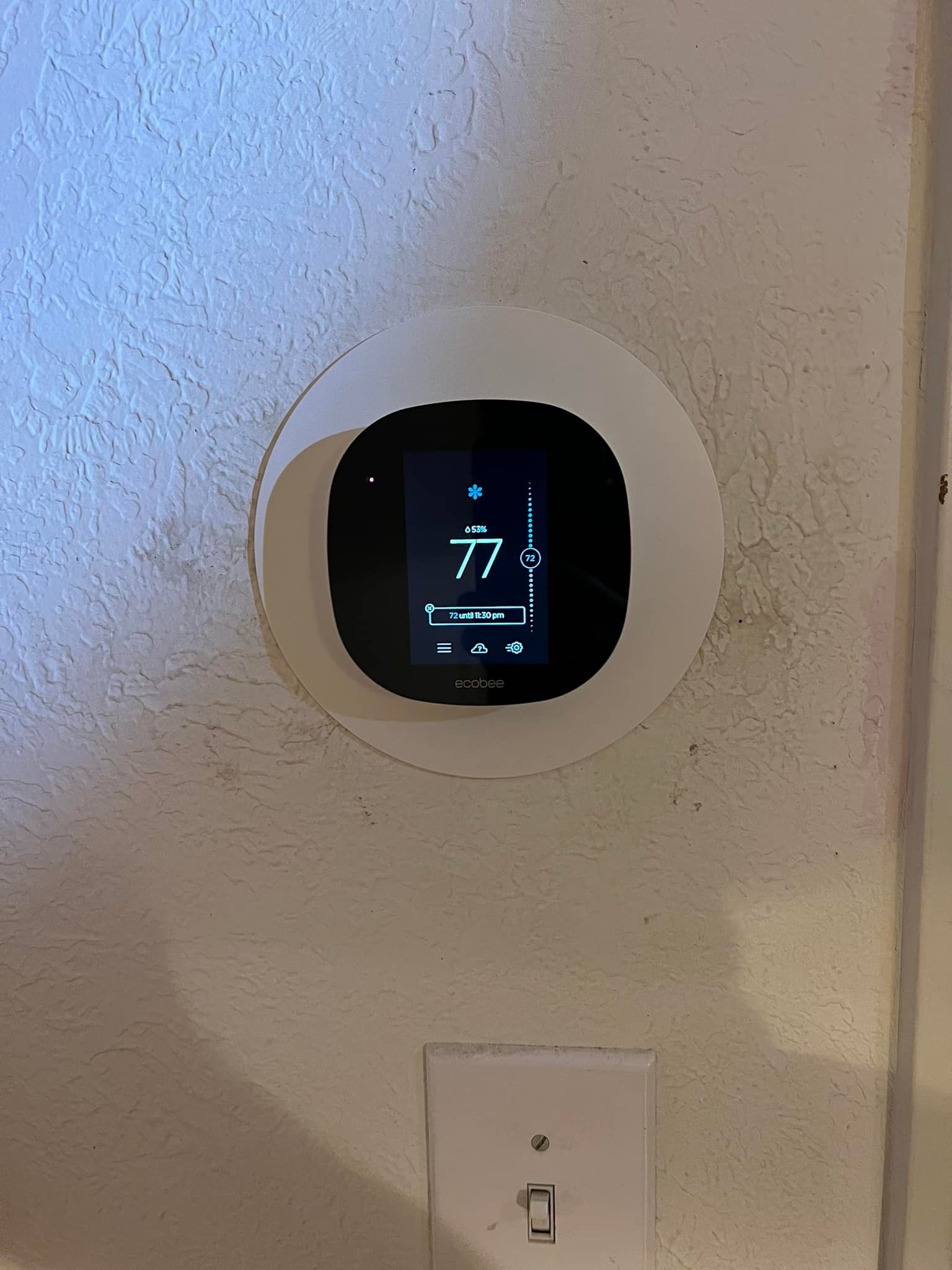 A thermostat is sitting on a white wall next to a light switch.