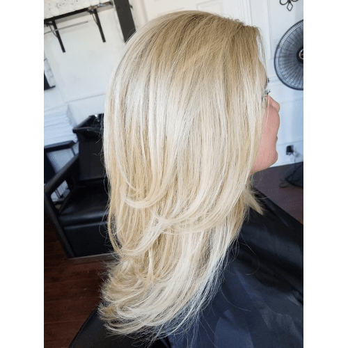A woman with long blonde hair is sitting in a chair in a salon.