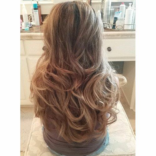 A woman with long hair is sitting on a stool in front of a mirror.