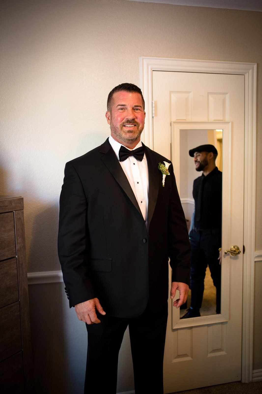 A man in a tuxedo is standing in front of a mirror.