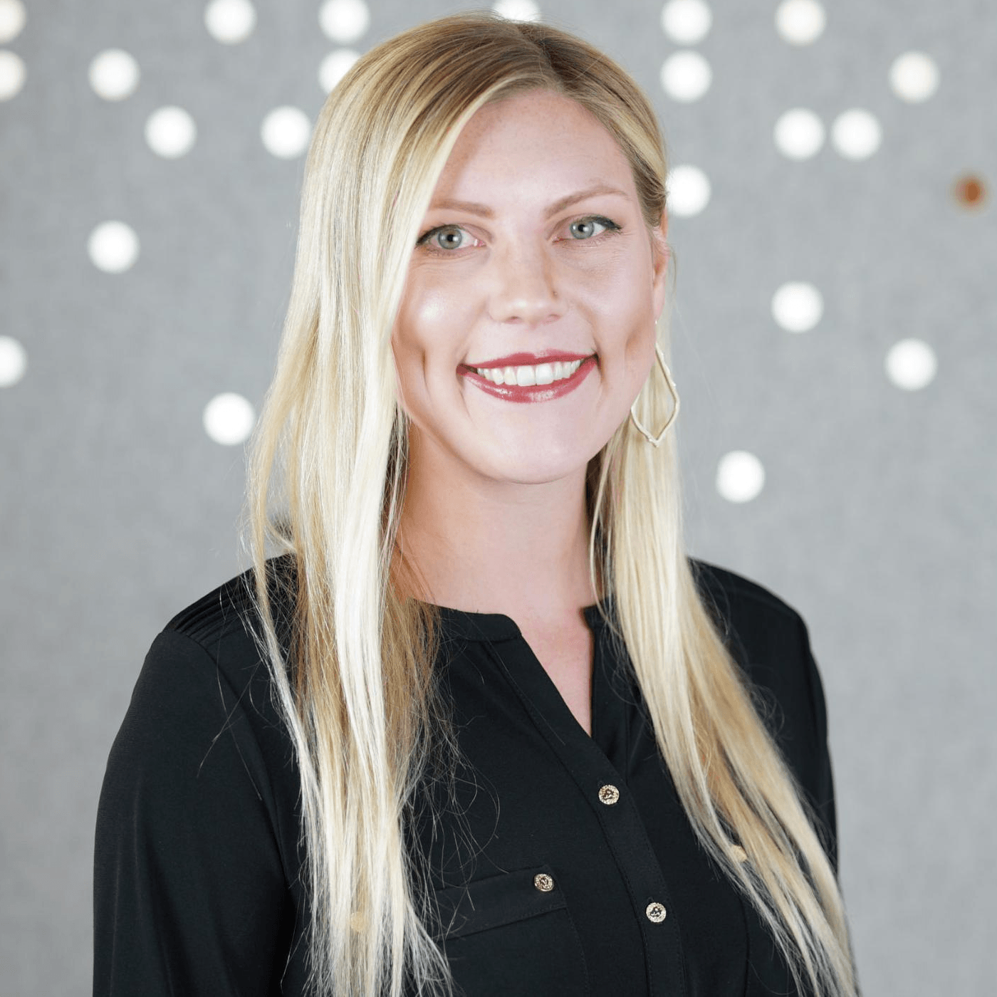 A woman with long blonde hair is wearing a black shirt and smiling.