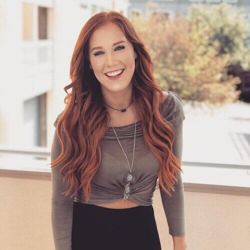 A woman with long red hair is smiling for the camera