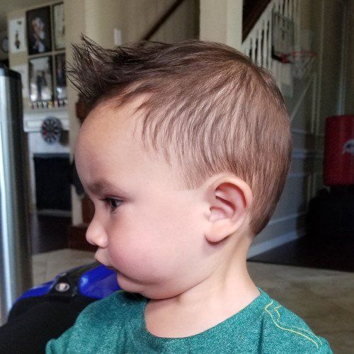 A young boy with a mohawk hairstyle is wearing a green shirt.