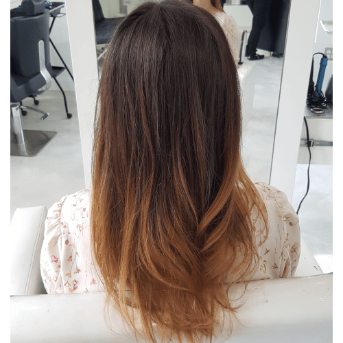 A woman with long hair is sitting in a chair in front of a mirror.