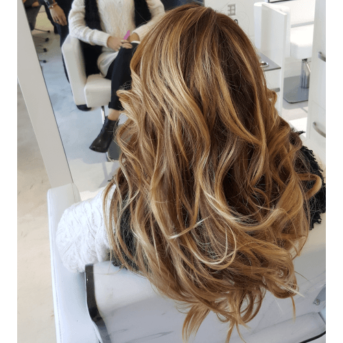 A woman with long wavy hair is sitting in a chair in front of a mirror.