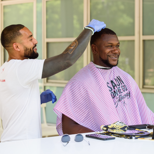 A man is getting his hair cut by another man wearing a shirt that says sau omega