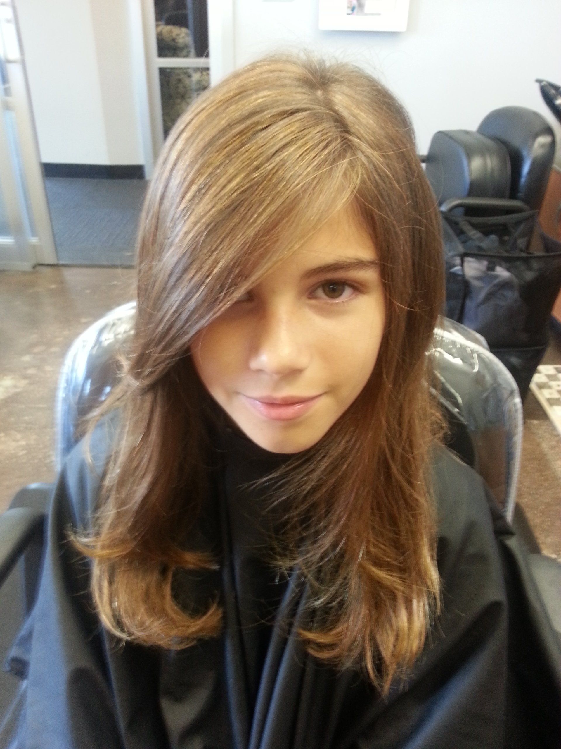 A young girl with long hair is sitting in a chair in a salon.