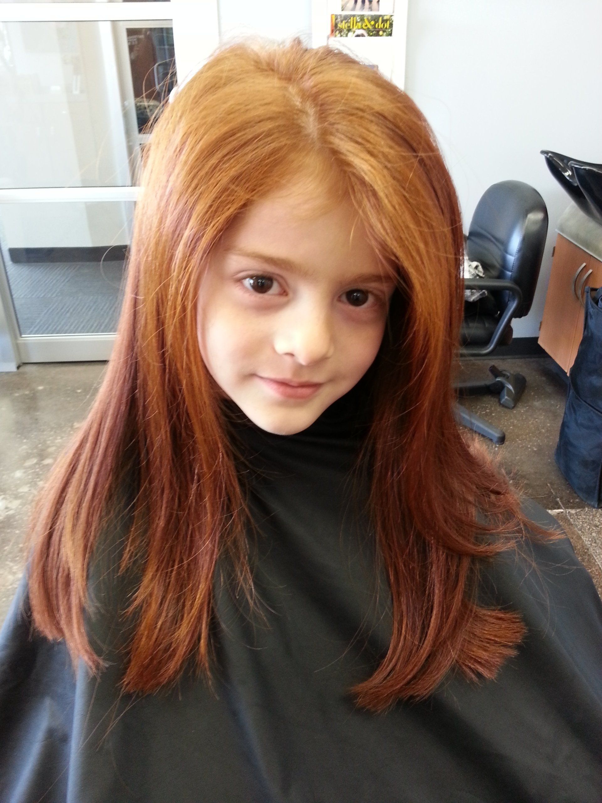 A little girl with long red hair is getting her hair cut