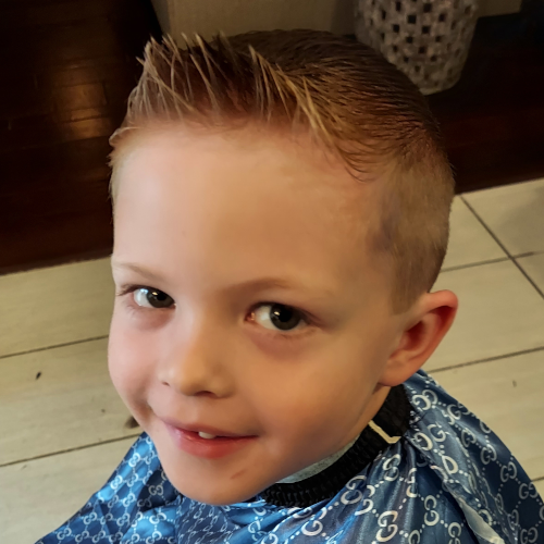 A young boy wearing a blue gucci cape smiles for the camera