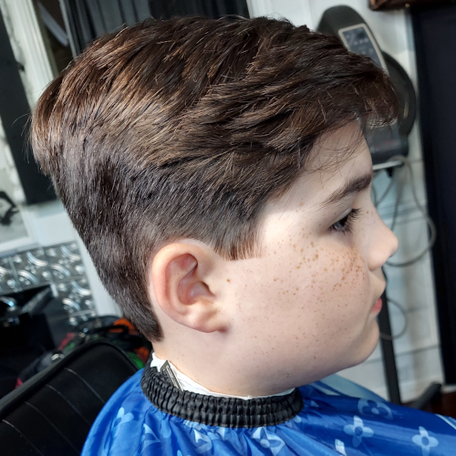 A young boy is getting his hair cut at a barber shop.
