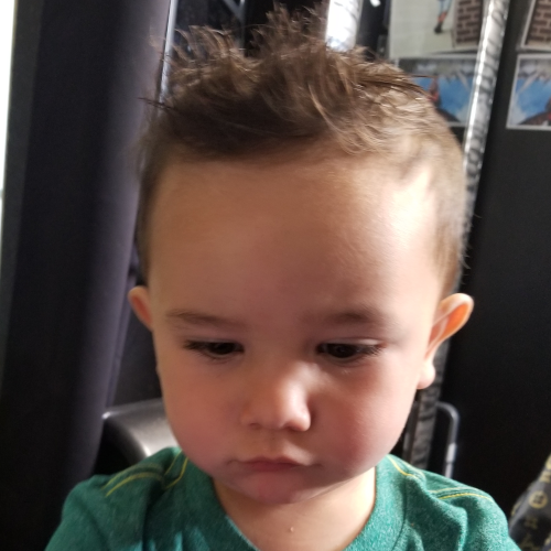 A baby with a mohawk hairstyle is wearing a green shirt
