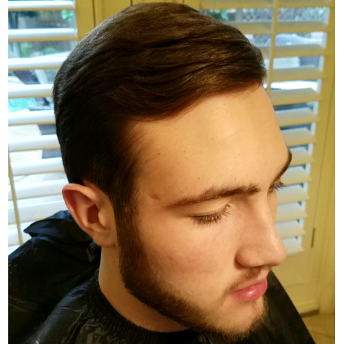 A man with a beard is getting his hair cut at a barber shop.