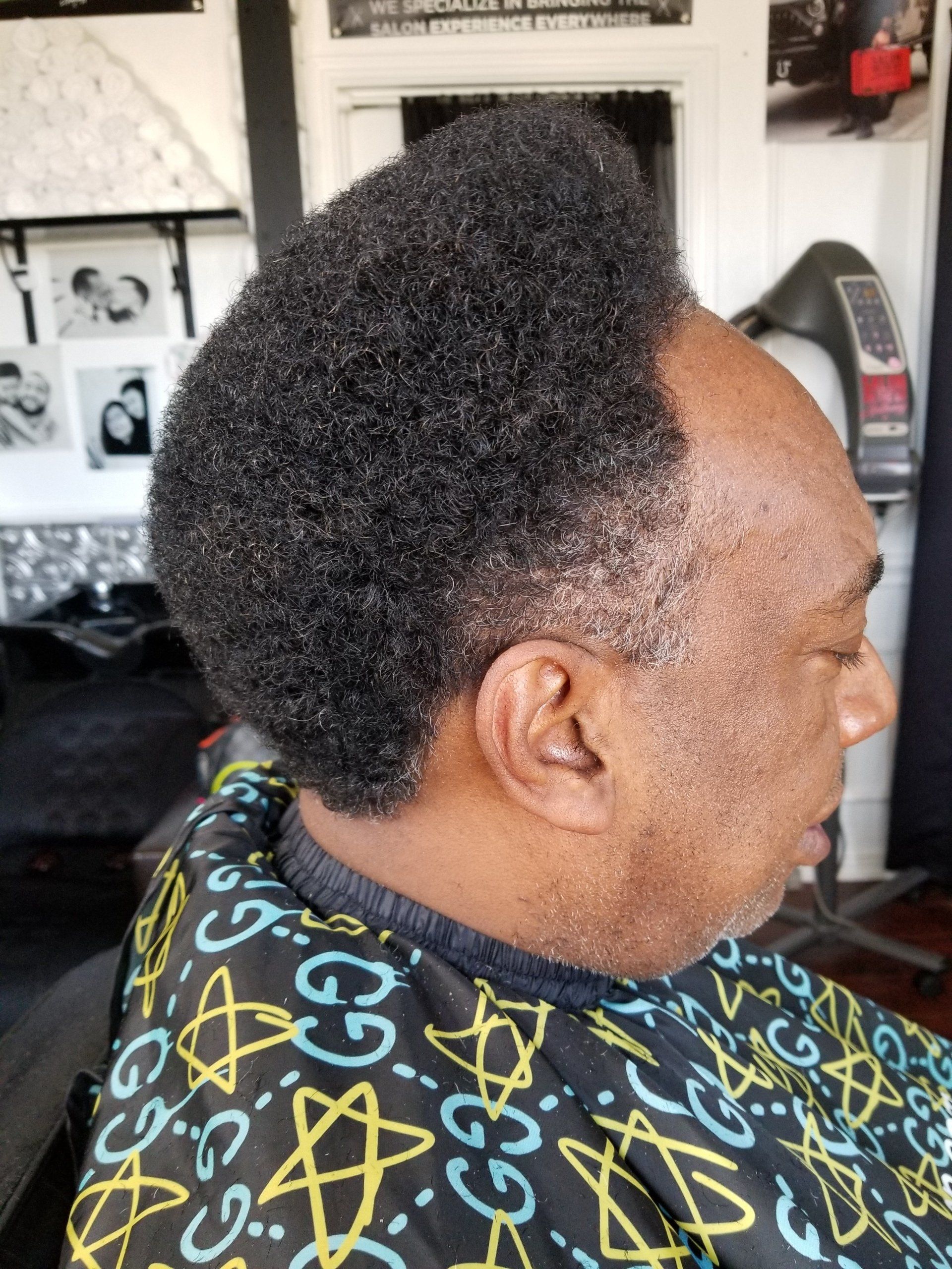 A man is getting his hair cut by a barber wearing a gucci apron.