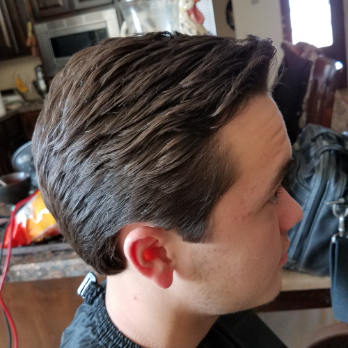 A man is getting his hair cut in a kitchen.