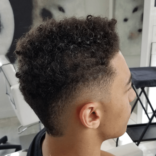 A young man with curly hair is getting his hair cut in a salon.