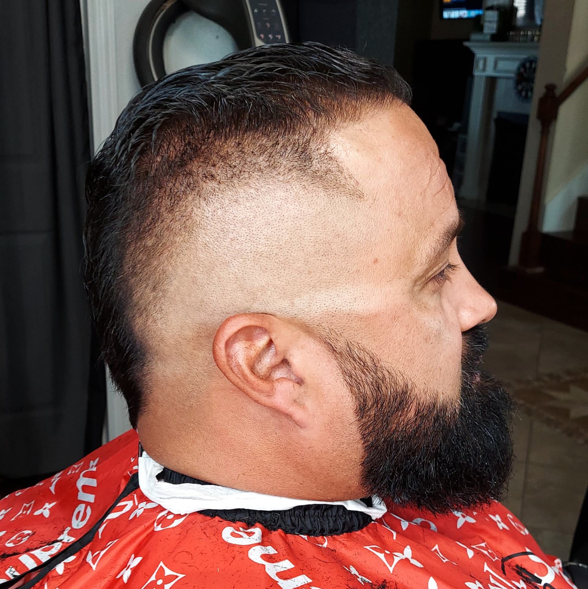 A man with a beard is getting his hair cut by a barber