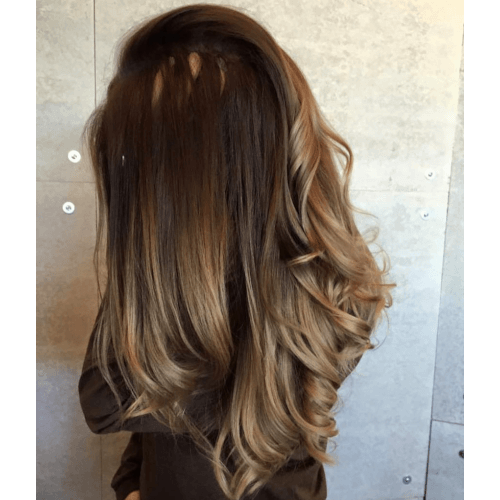 A woman with long brown hair is standing in front of a wall.