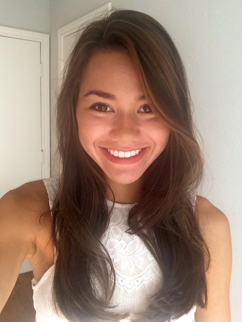 A woman is smiling for the camera while wearing a white tank top.