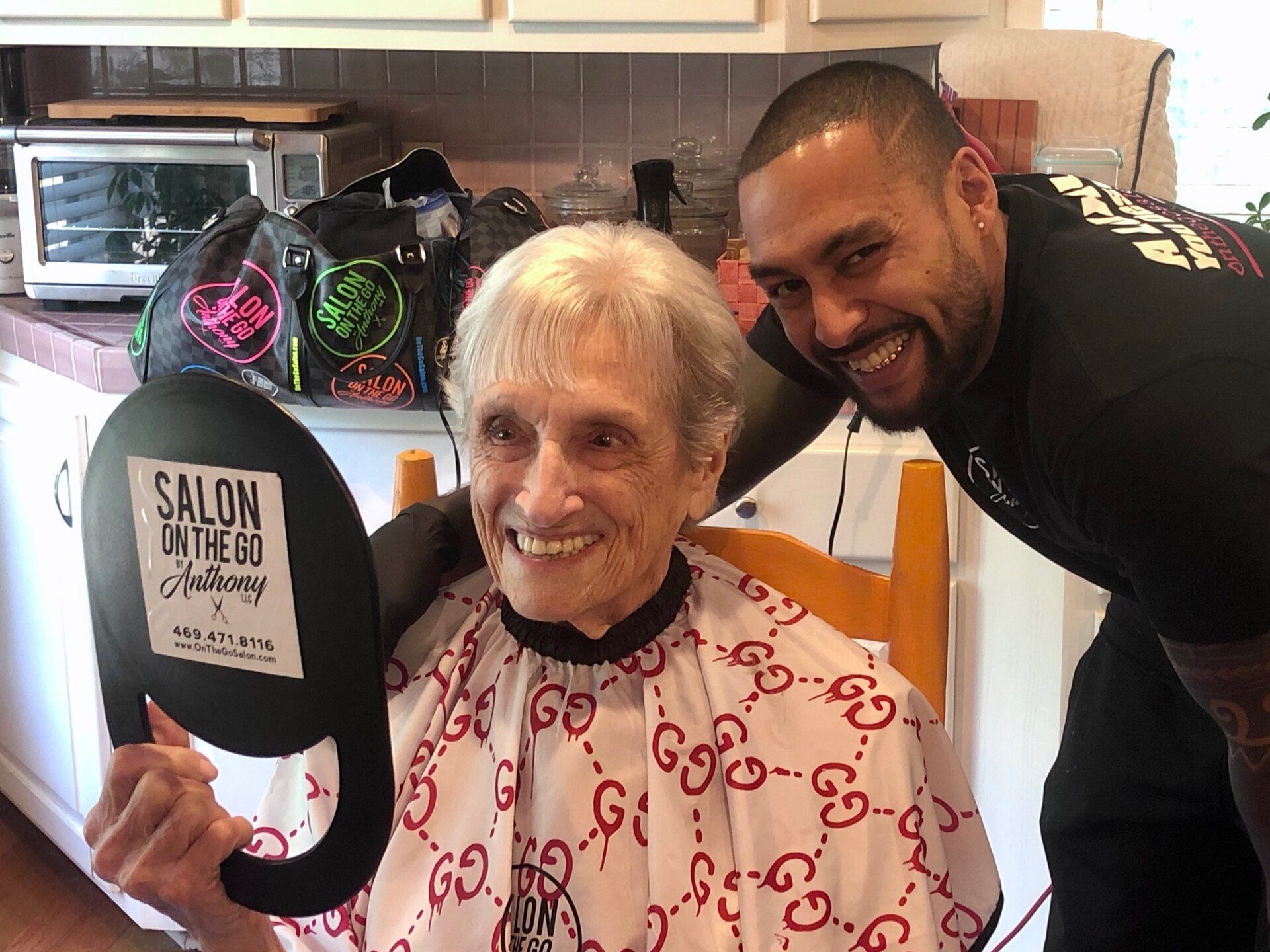 A man is standing next to an elderly woman getting her hair cut.