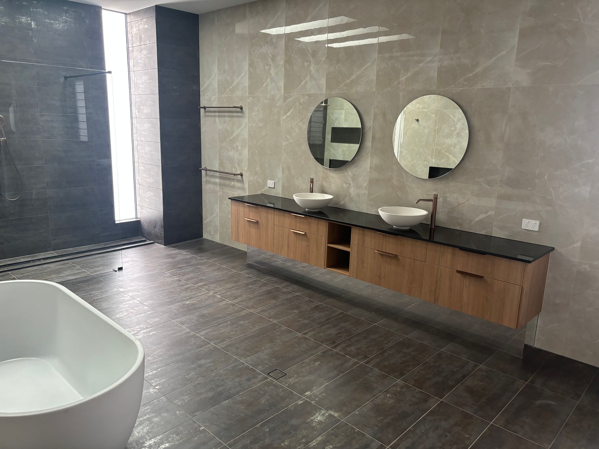 A bathroom with 2 circle mirrors a grey tile and a cabinet with sinks — Cairns Custom Wardrobes in Manunda, QLD