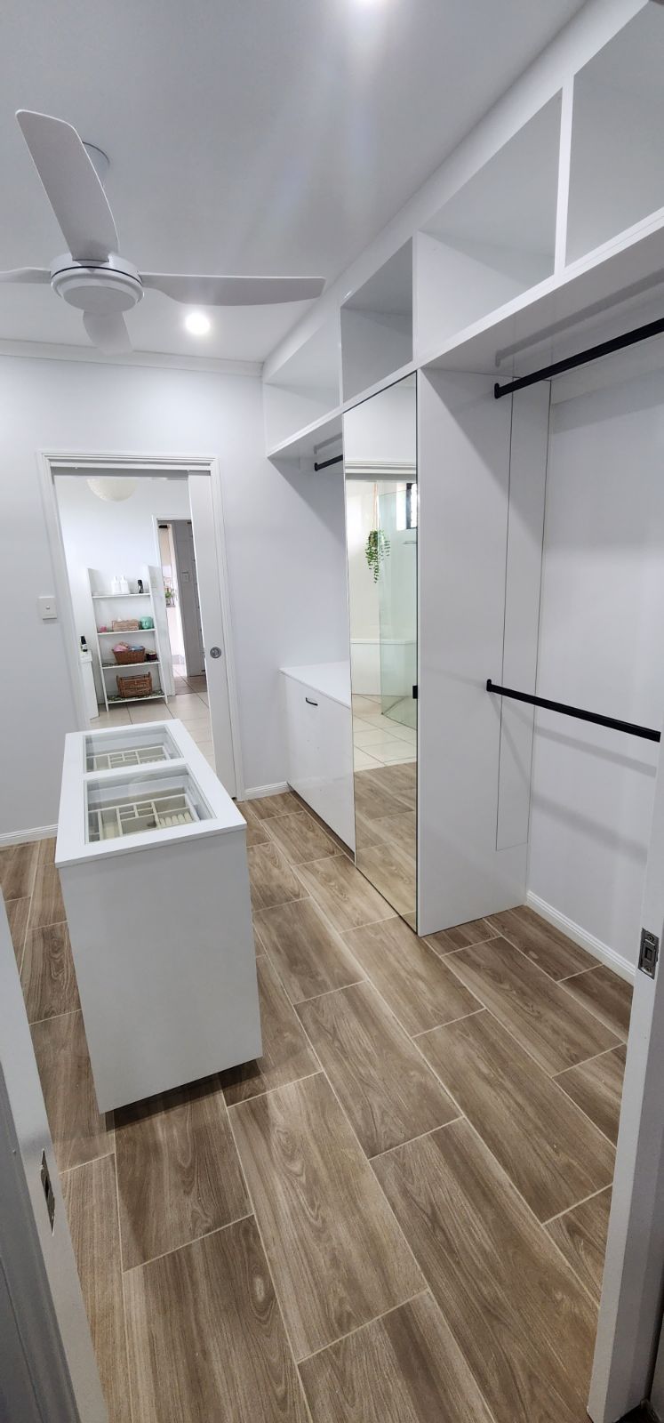 a walk in wardrobe with a bathroom in the background and a wooden floor  — Cairns Custom Wardrobes in Manunda, QLD