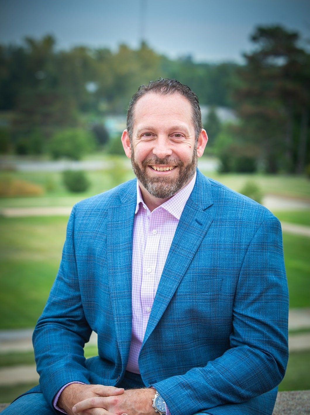 A man in a blue suit and pink shirt is sitting on a rock.