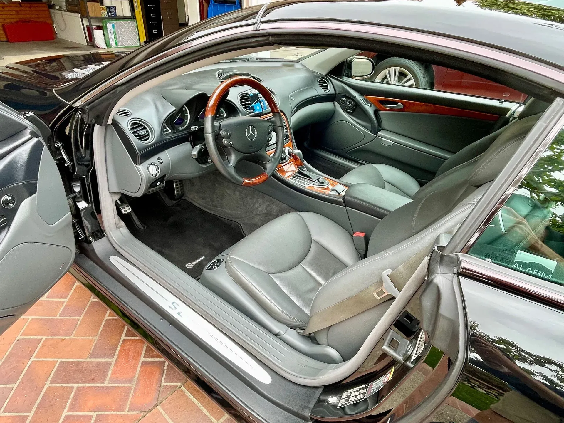 A black car with the driver's side door open, showing a gray leather interior with wood trim and a steering wheel.