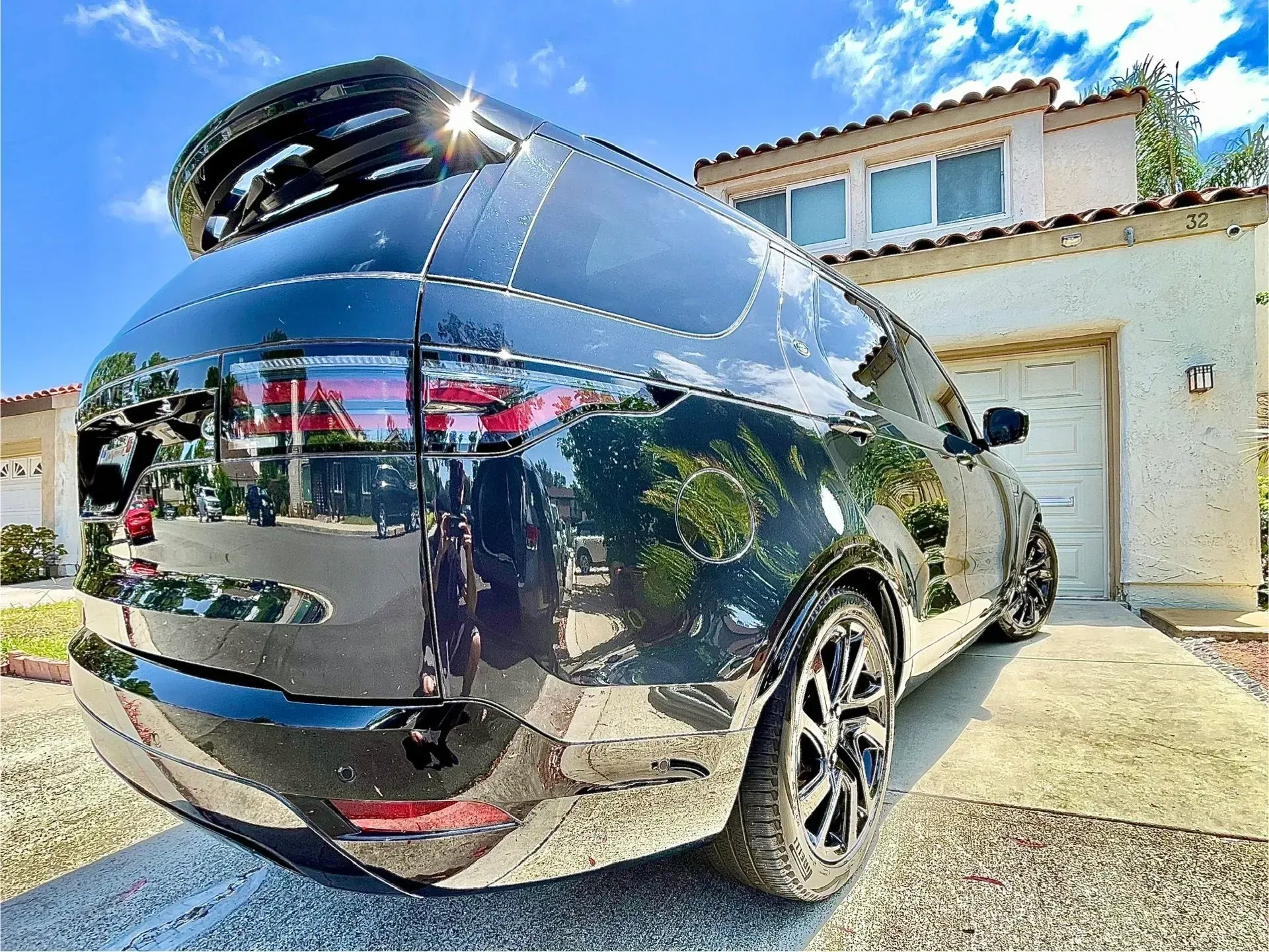 A shiny black SUV parked in a driveway in front of a house under a clear, bright blue sky.