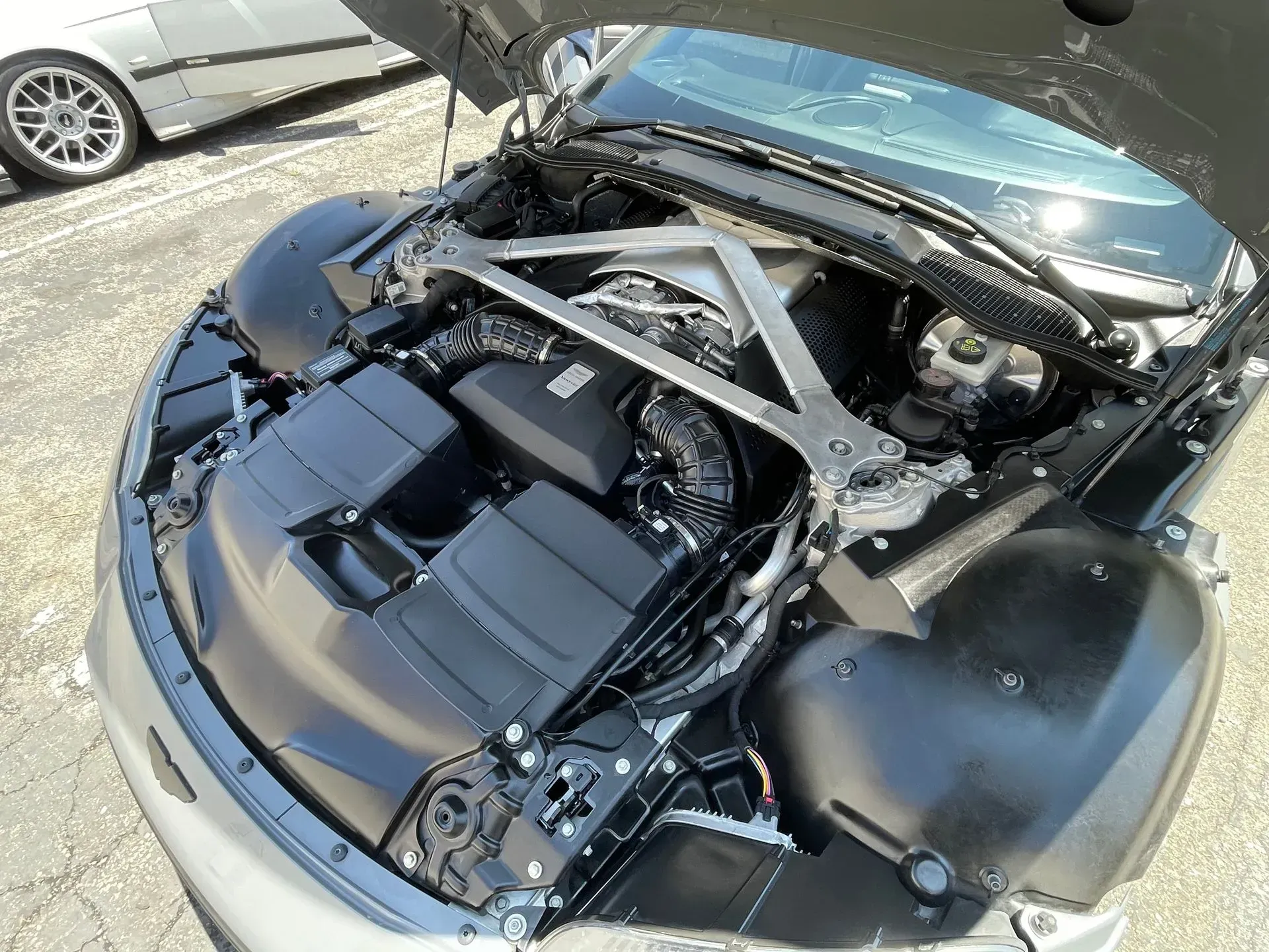 An open hood of a high-performance sports car, revealing a powerful engine with a metal strut brace, seen from above.