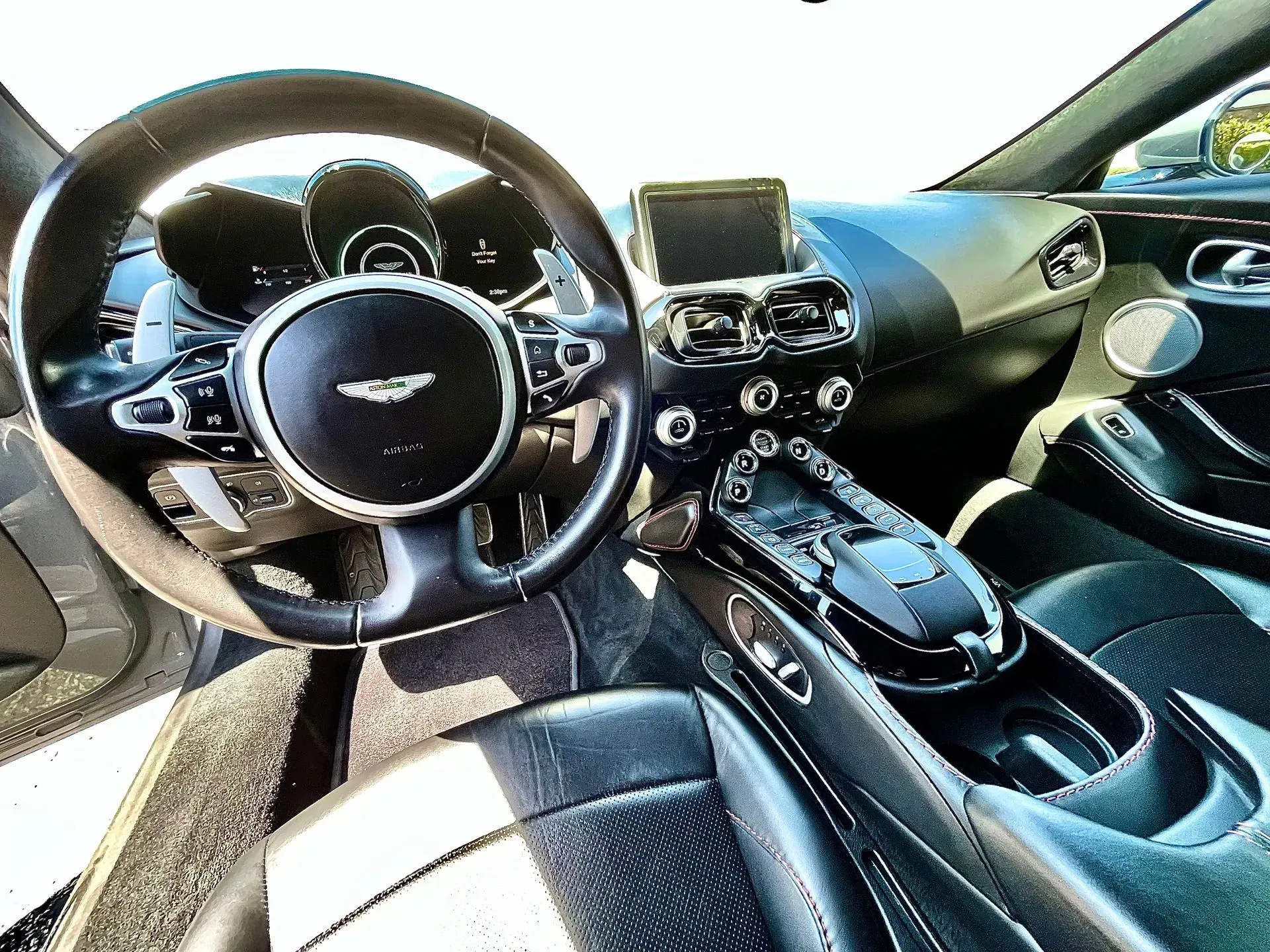 Interior view of a black Aston Martin cockpit, highlighting the leather steering wheel, center console, and dashboard.